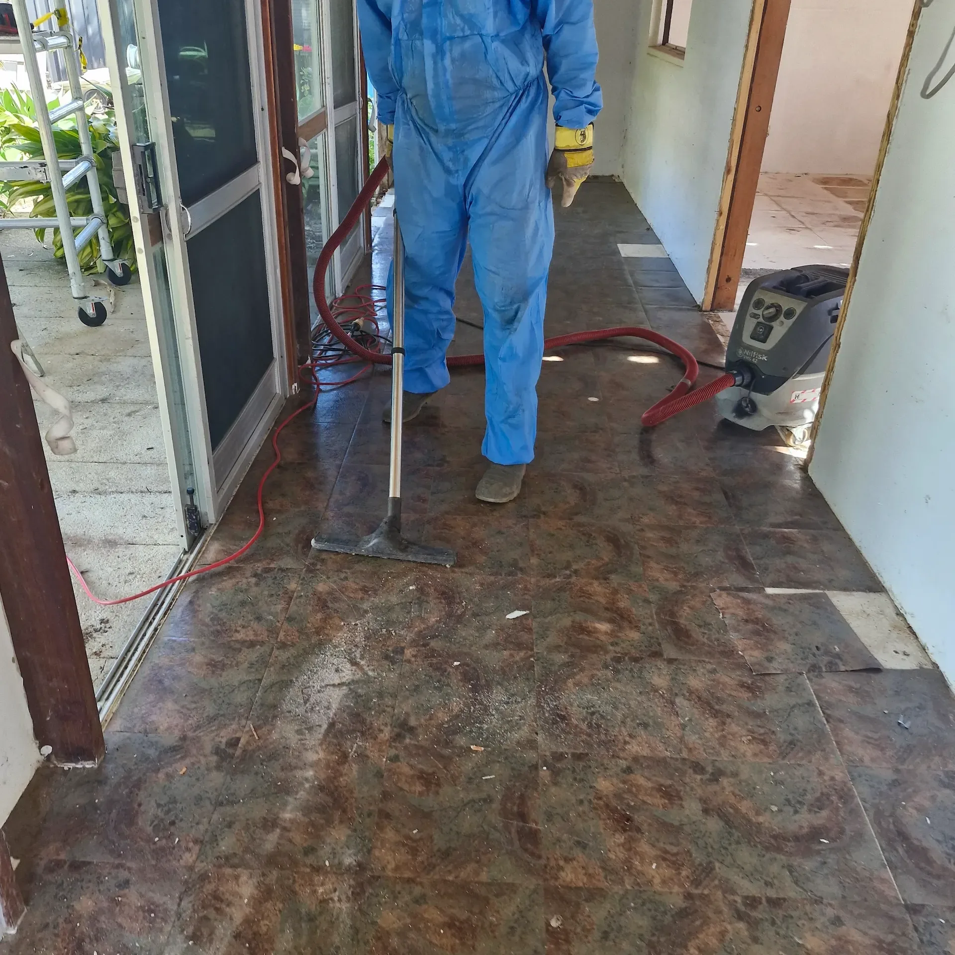 Worker in blue protective coveralls carrying out floor removal inside a house