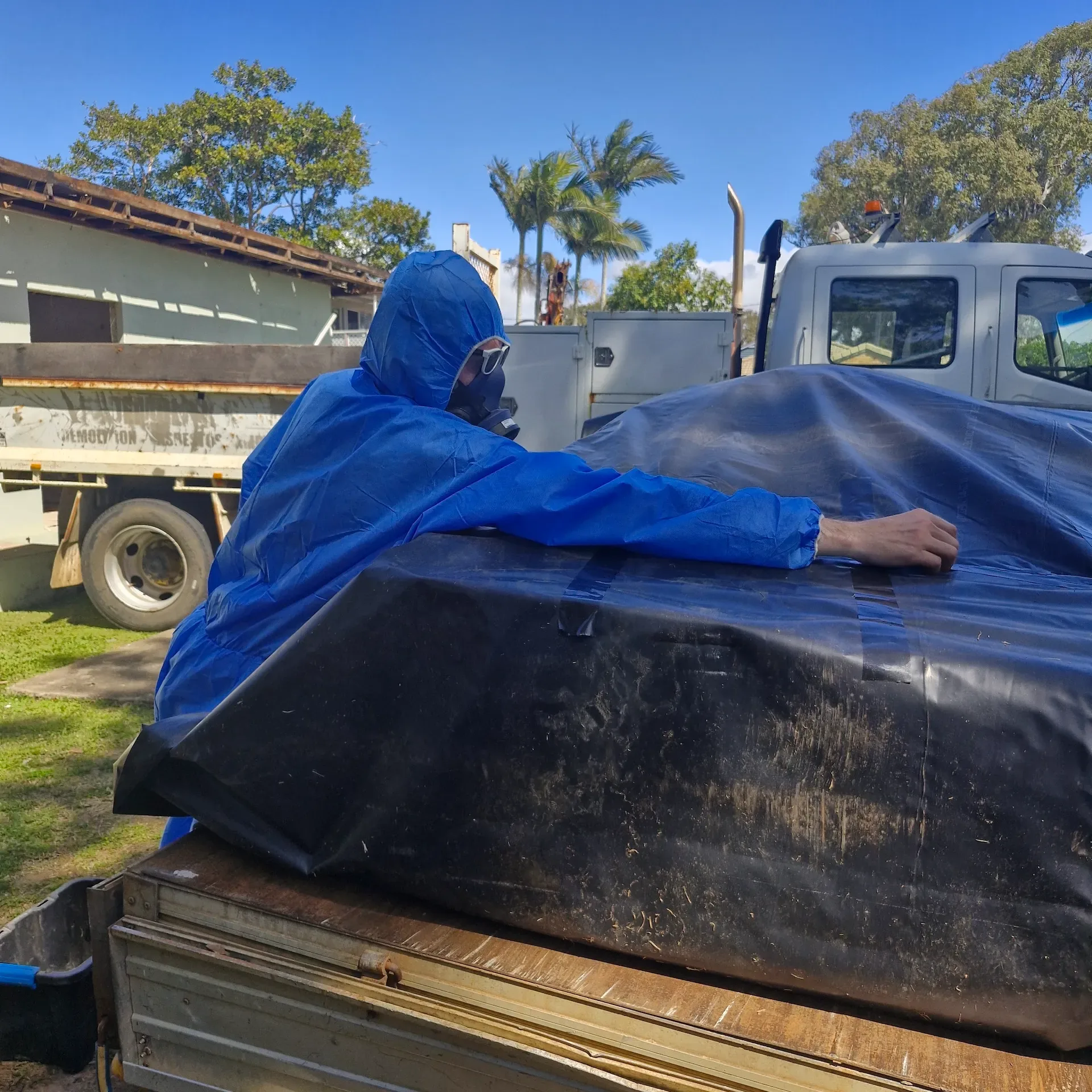 Worker in blue protective coveralls handling a wrapped building sheet beside a utility vehicle