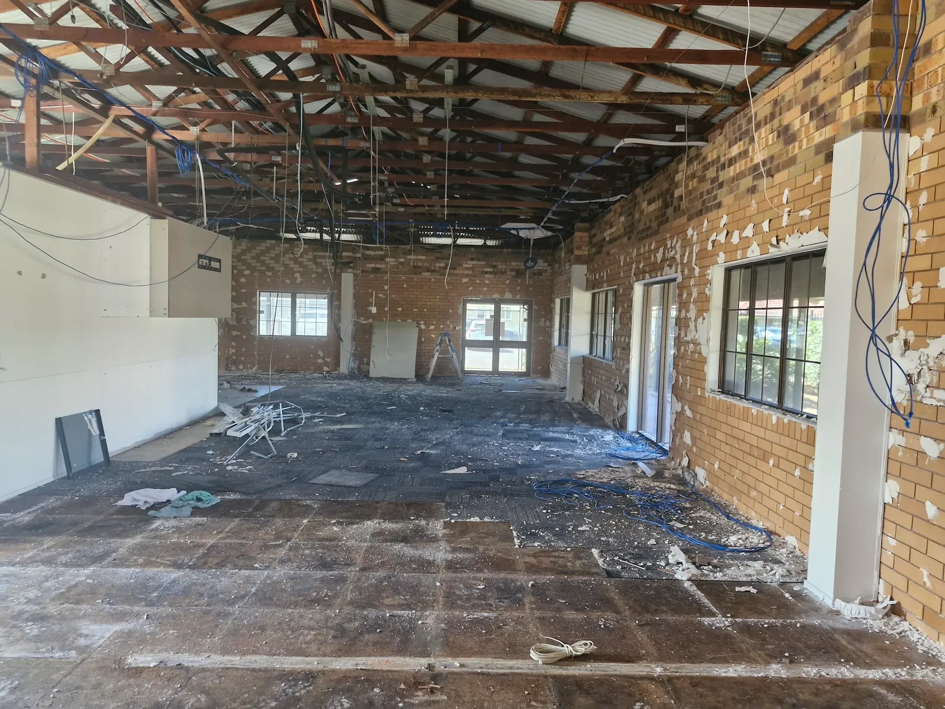 Interior of a building stripped back to brick walls, roof framing and bare floor during demolition work