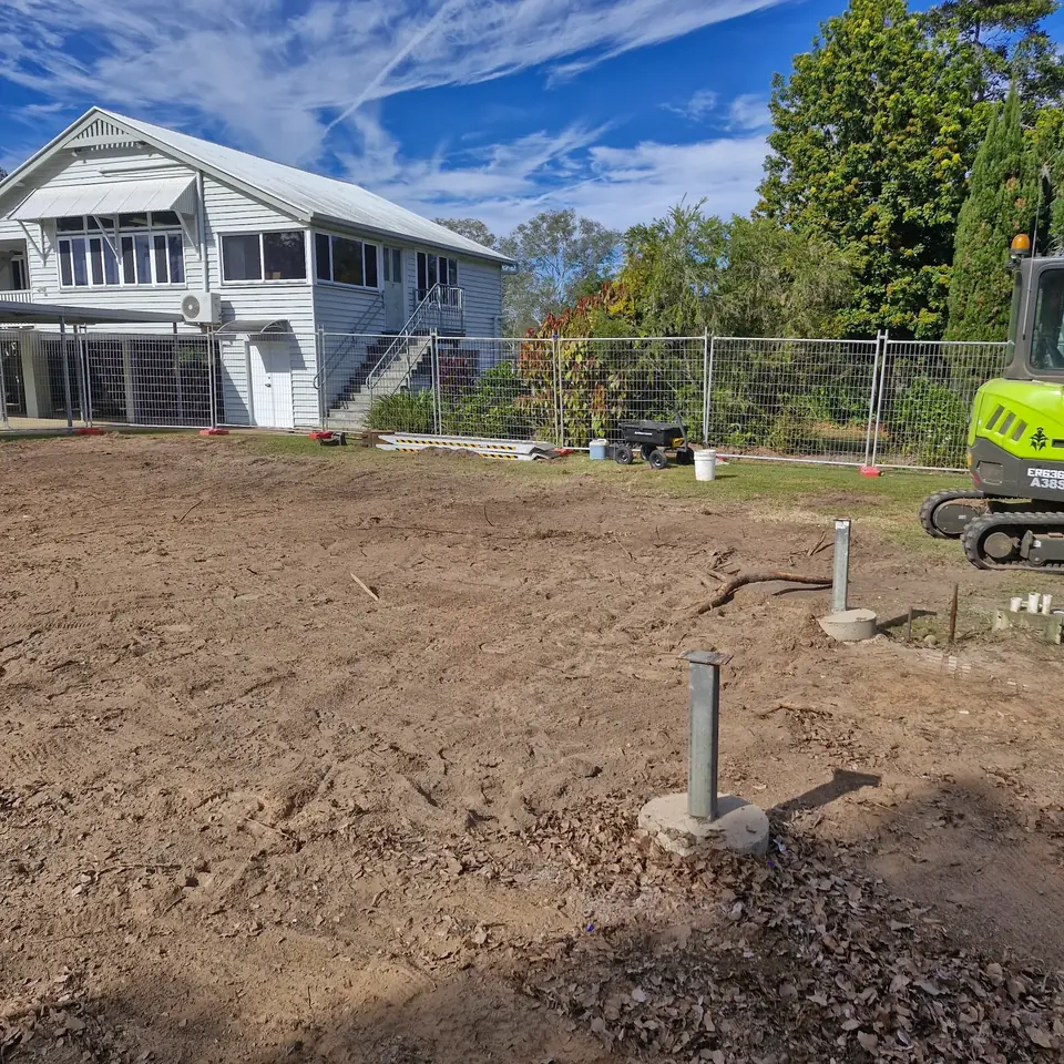 Cleared residential site with exposed ground beside a raised timber home