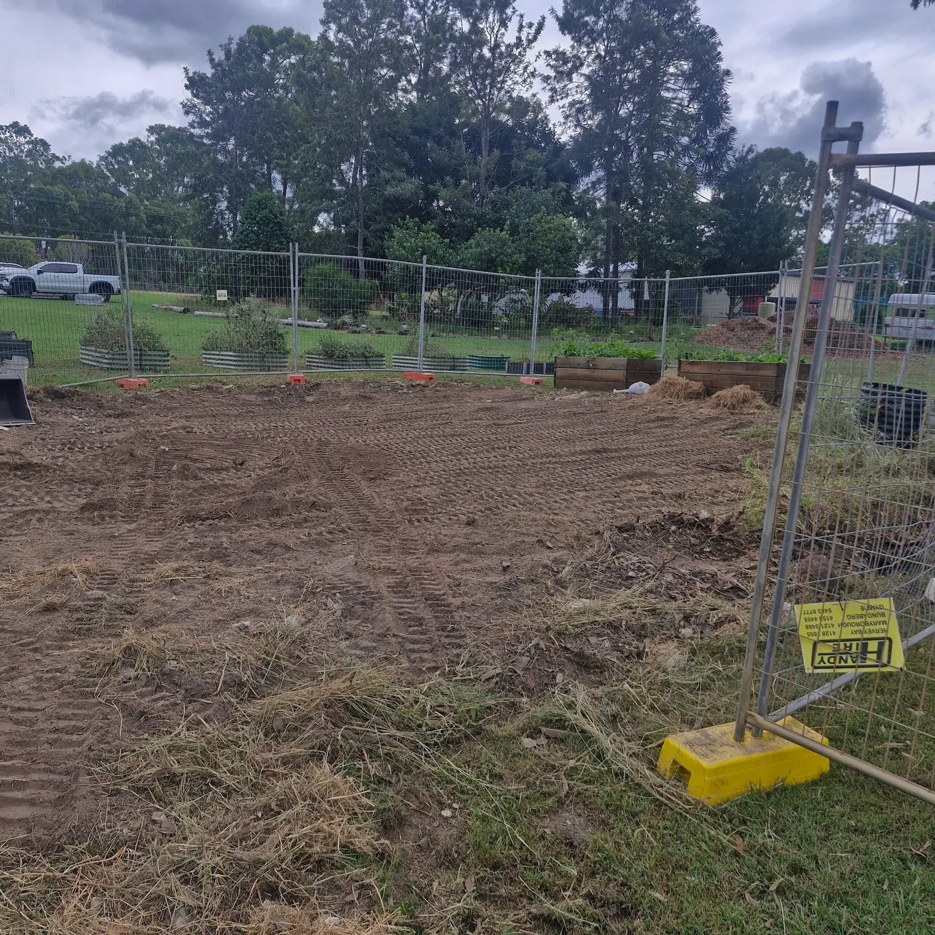 Cleared worksite with disturbed soil, temporary fencing and trees beyond