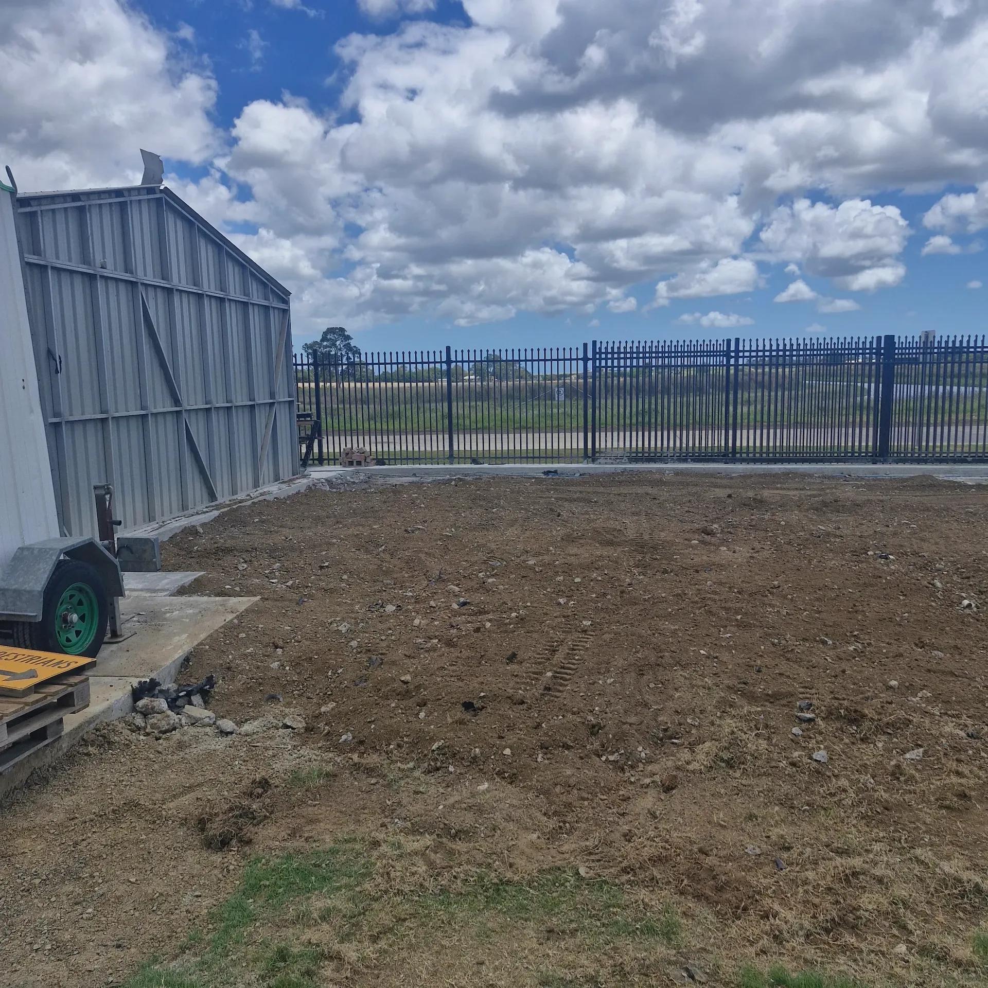 Cleared ground beside a shed and perimeter fencing under a cloudy sky