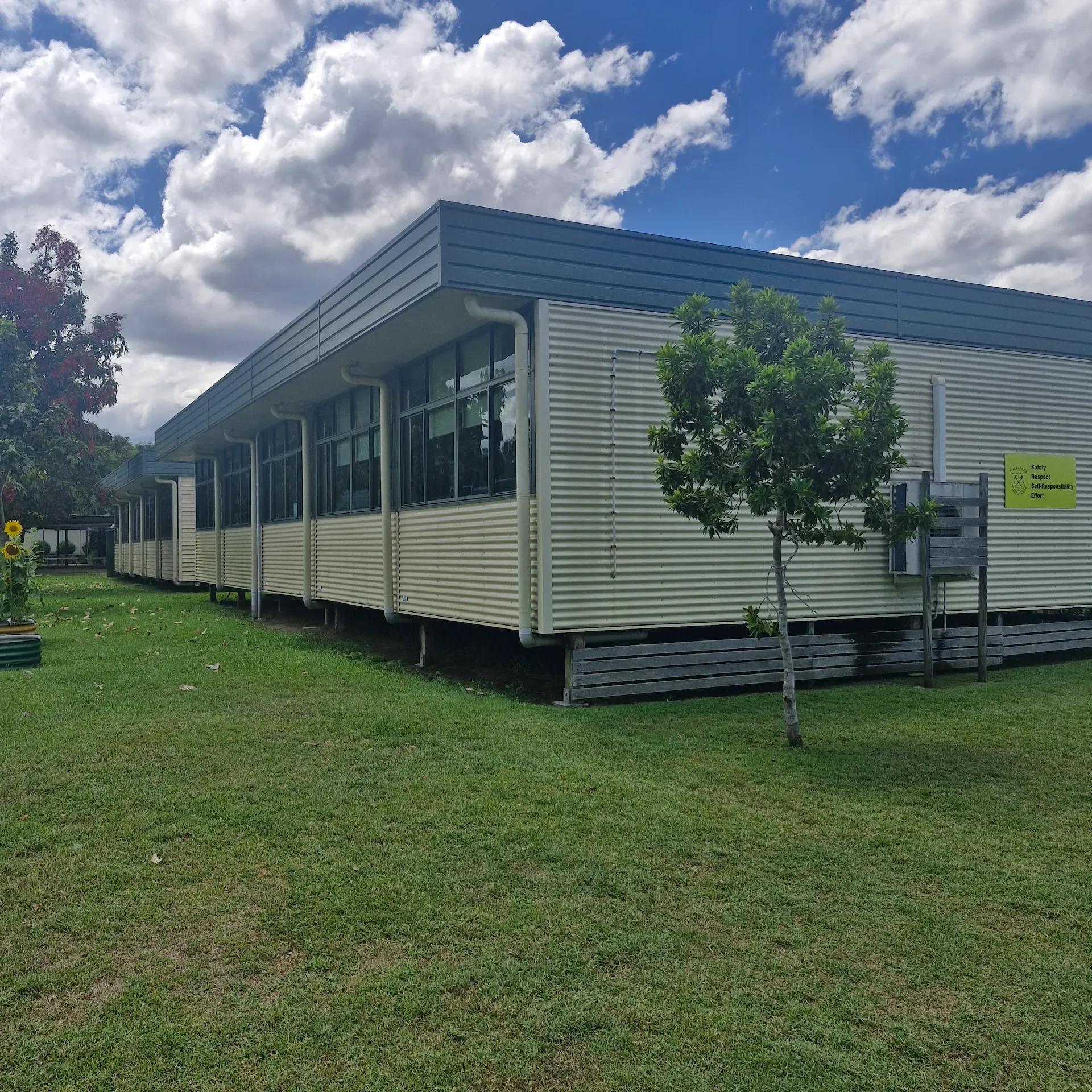 Long single-storey building on a grassed site beneath a cloudy sky
